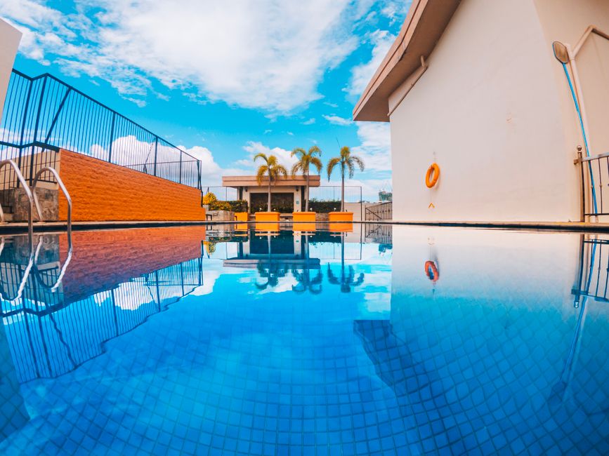 Stunning clear blue swimming pool reflecting palm trees and tropical sky.